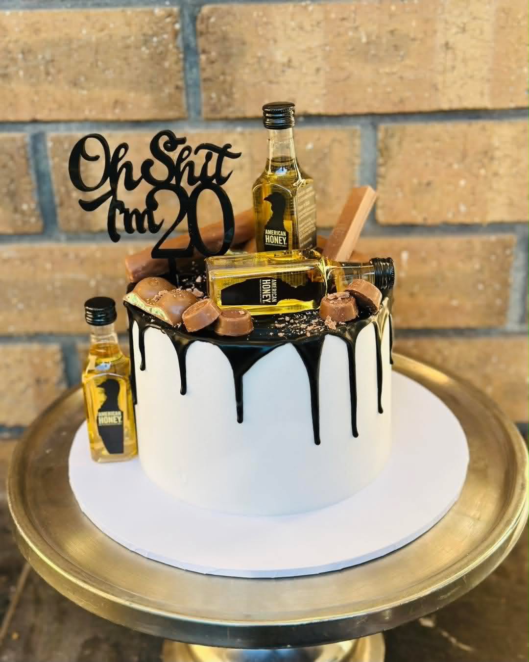 White cake with black chocolate drip, mini whiskey bottles, Rolo chocolates and Oh Shit I'm 20 topper